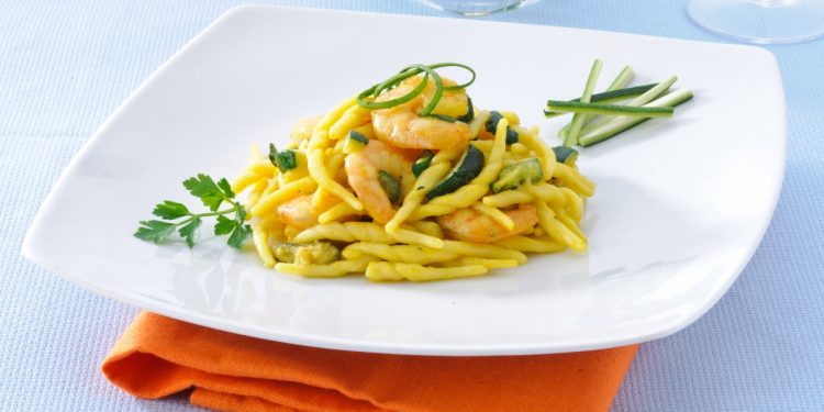 su tavolo di marmo, piatto bianco con un tovagliolo arancione, nel piatto trofie con zucchine e gamberetti