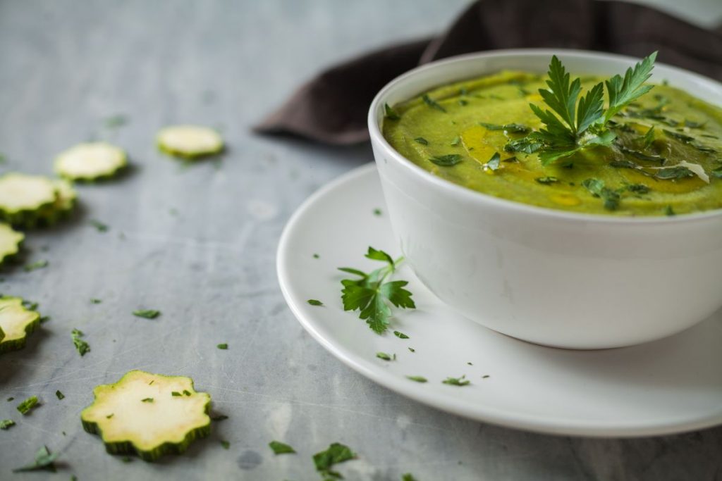 su base grigia piattino e tazza da brodo bianca piena di vellutata di zucchine. Rondelle di zucchine sparse