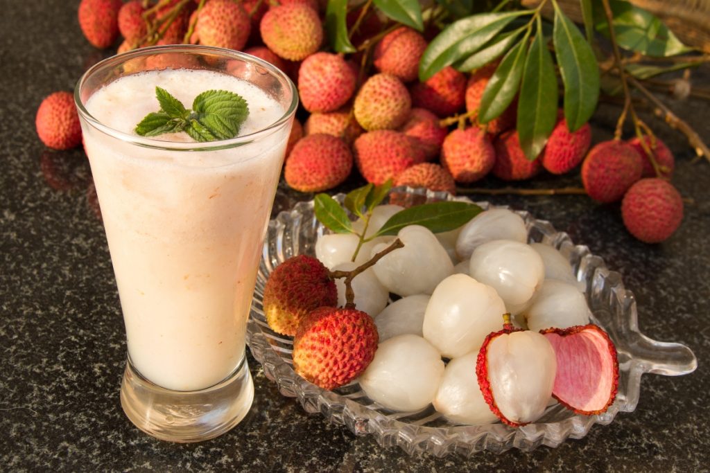 piatto in vetro con litchi sgusciati, e litchi interi sullo sfondo, un bicchiere con succo bianco