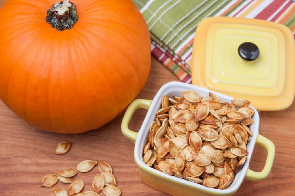 teglia con manici con semi di zucca tostati accanto a una grossa zucca