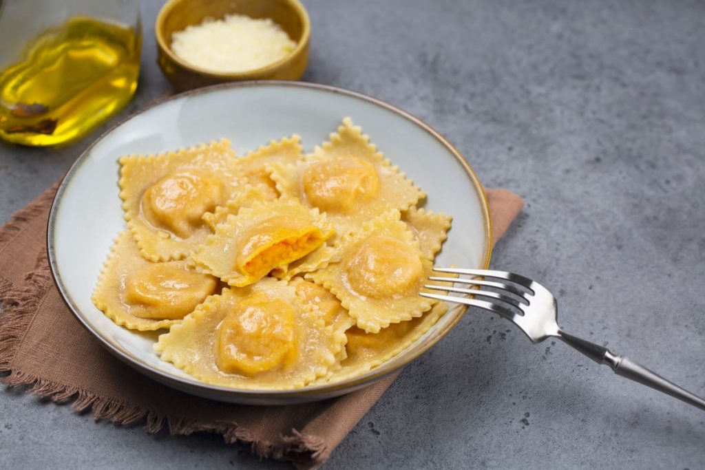 piatto fondo con tortelli di zucca, forchetta, olio e parmigiano accanto