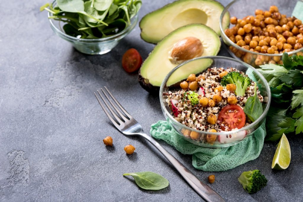 Piatto con ceci, insalata e avocado. Sul tavolo ingredienti per preparare ricette vegetariane