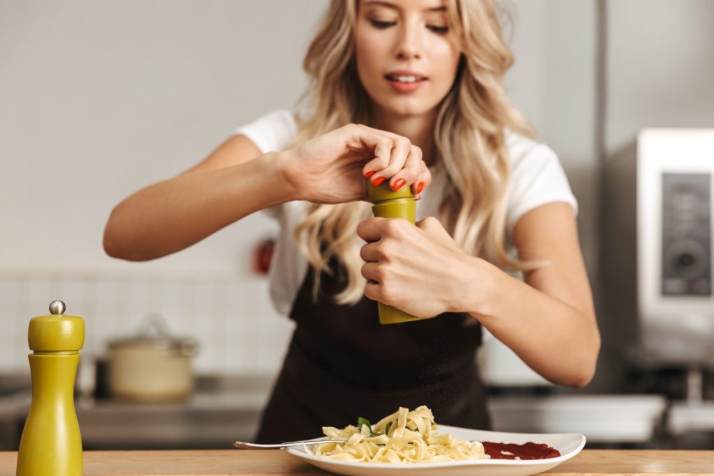 Donna che usa macina pepe sopra un piatto di pasta