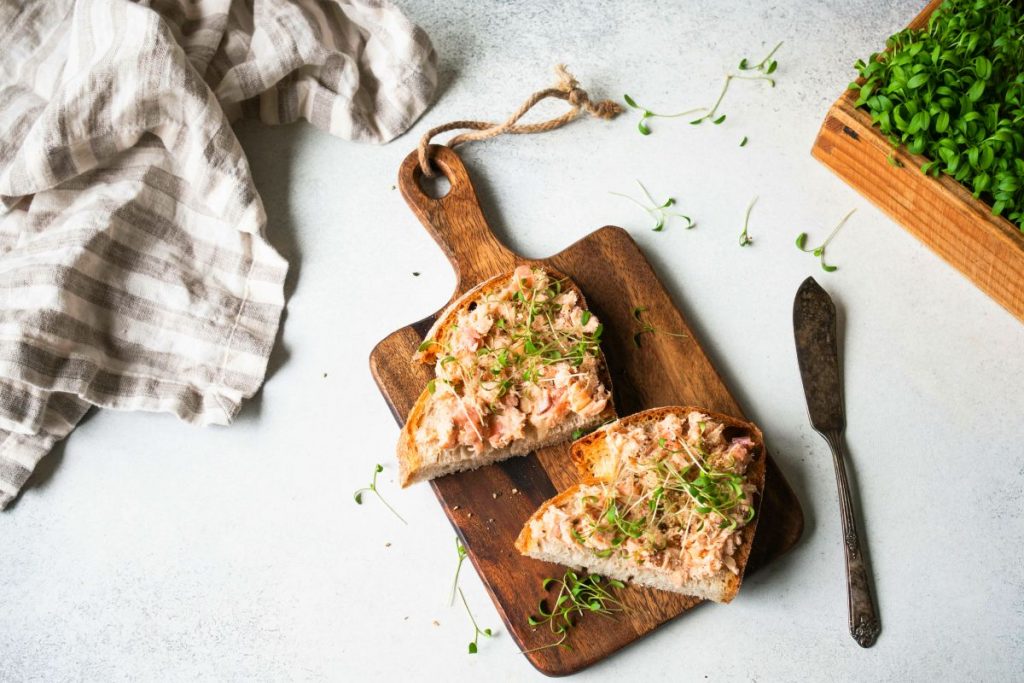 su tavolo di marmo, tagliere con 2 tartine di mousse di salmone, un coltello, un canovaccio e prezzemolo tritato