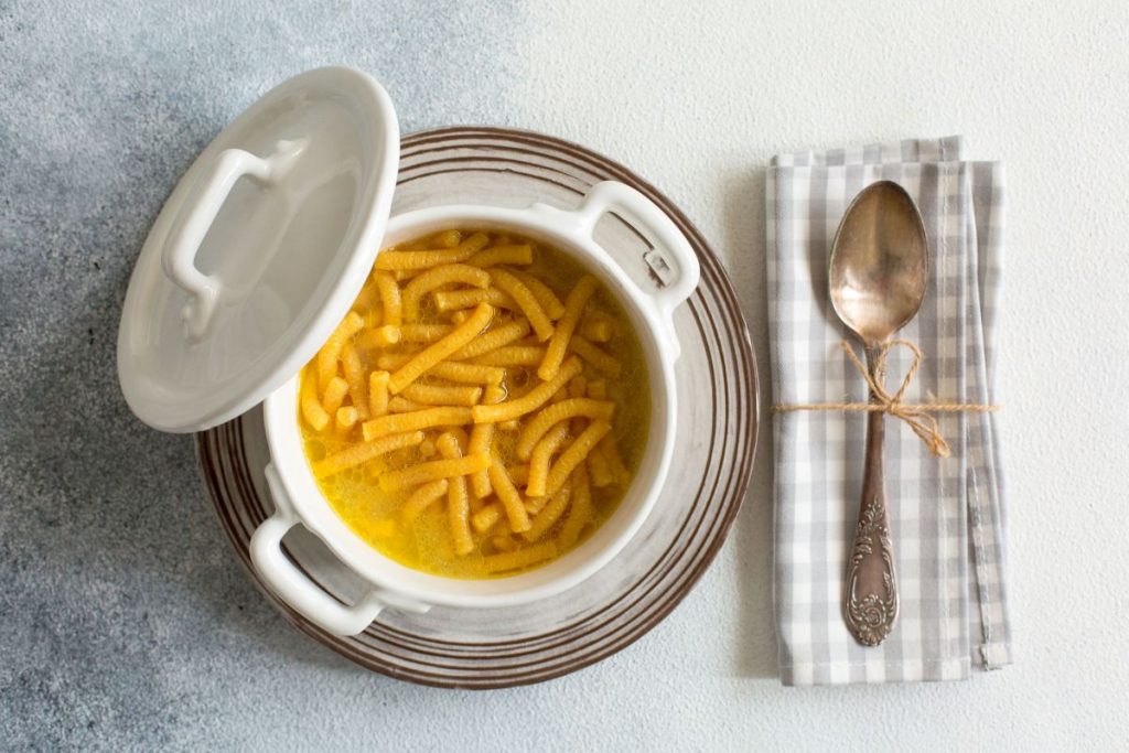 su tavolo di marmo . piatto di argento con una zuppiera che contiene i passatelli in brodo . Sulla destra un tovagliolo di cottone con un cucchiaio legato con un filo con carta