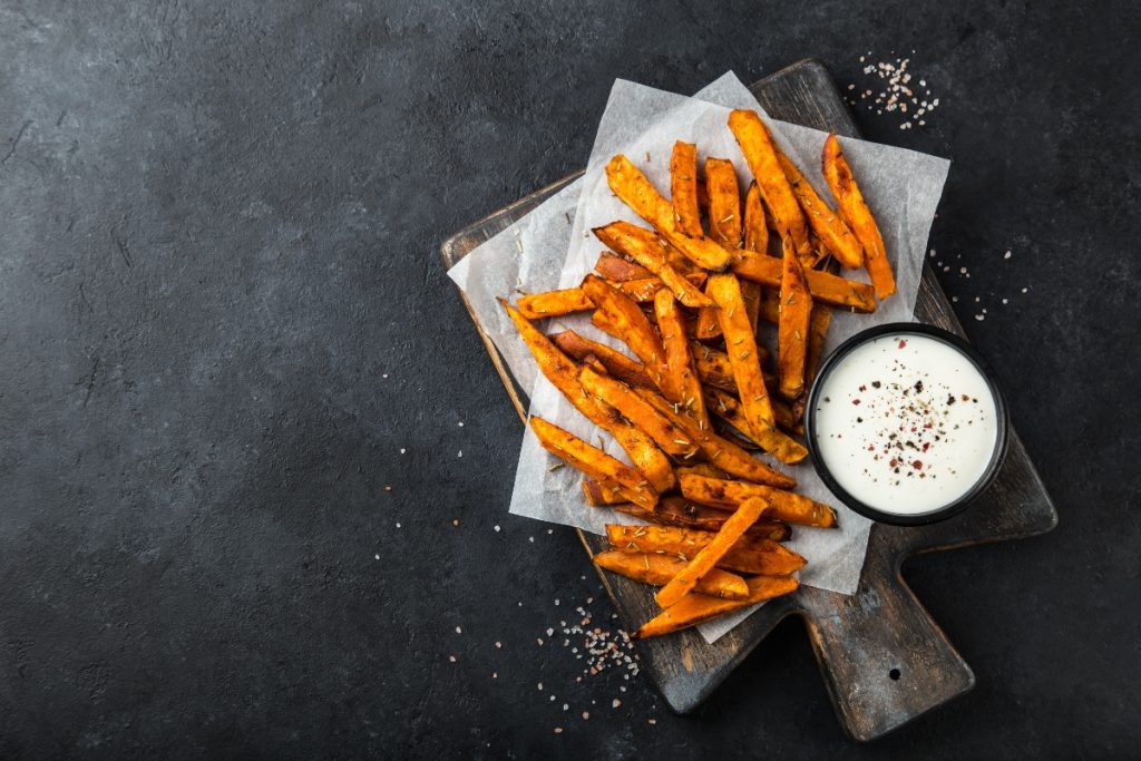 bastoncini di patate dolci fritte su un tavolo con accanto una ciotolina con della salsa