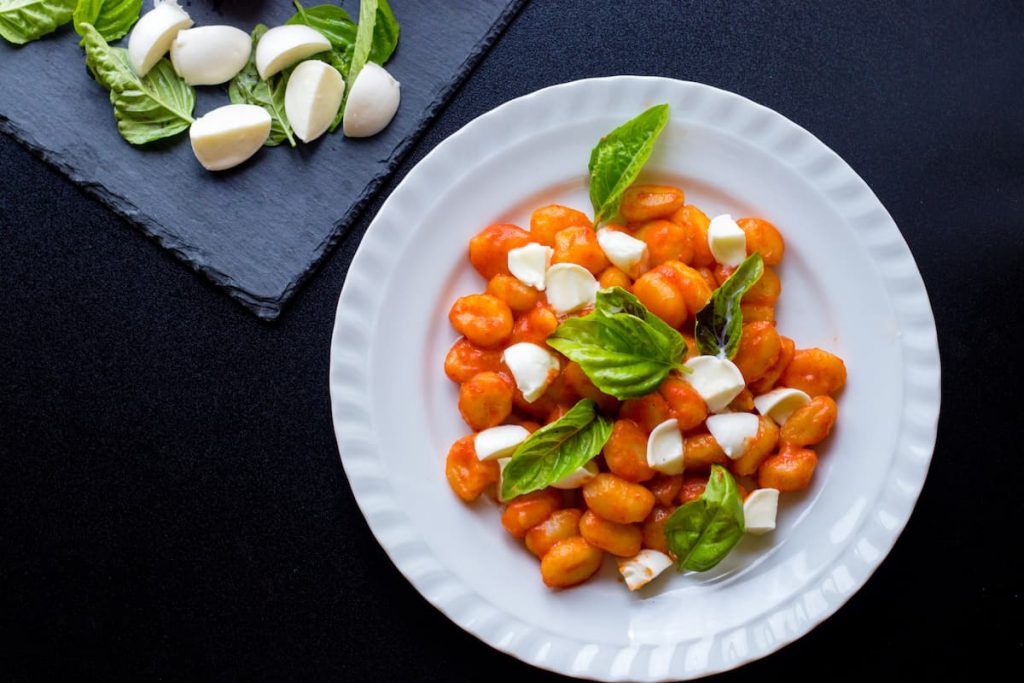 su sfondo nero, un piatto bianco con gli gnocchi alla Sorrentina con salsa di pomodori e mozzarella