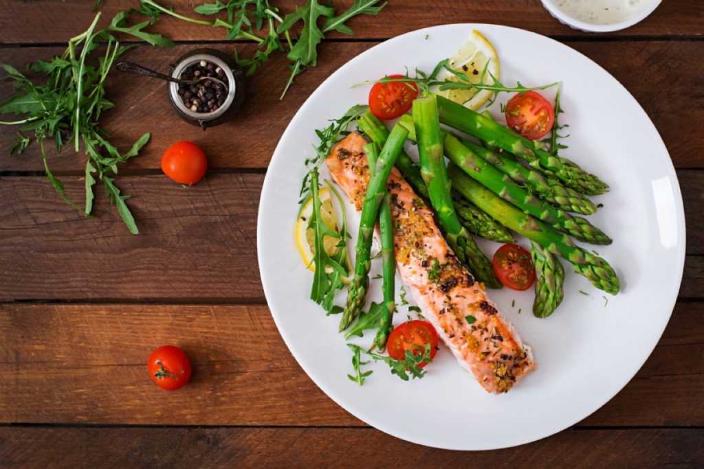 piatto su tavola di legno con trancio di salmone, asparagi e pomodorini