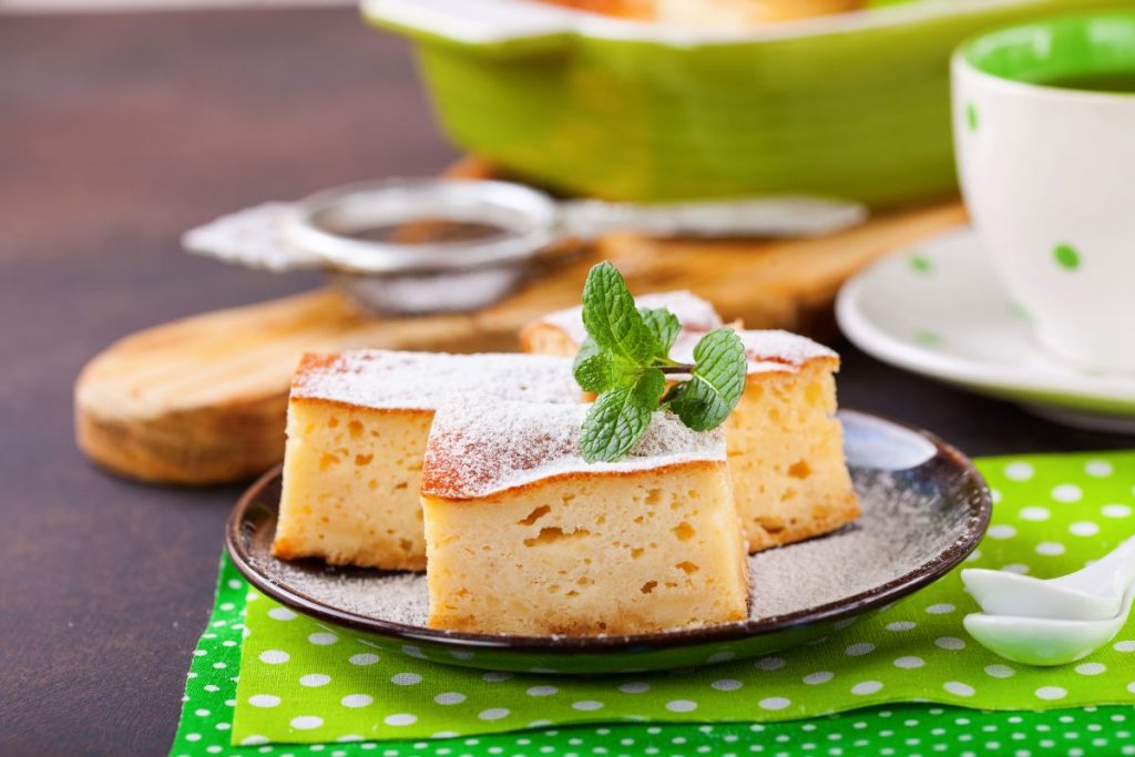 su tavolo apparecchiato per la colazione sotto piatto verde a pois bianco con un piatto nero e torta alla ricotta con un foglio di menta. accanto una tazza di tè