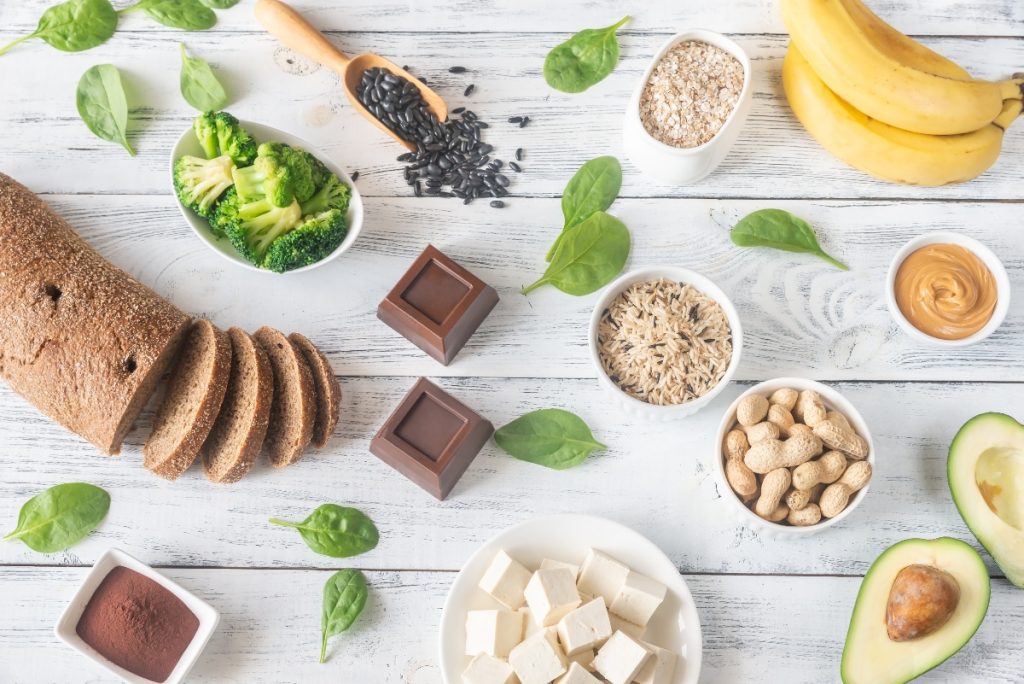 su tavolo di legno bianco alimenti ricchi di magnesio come pane integrale cioccolato fondente, banana e avocado