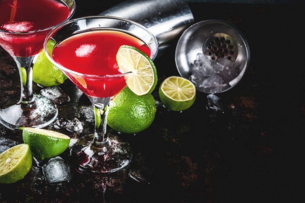 due calici con cocktail rosso Sosmolitan, fettine di lime e spicchi