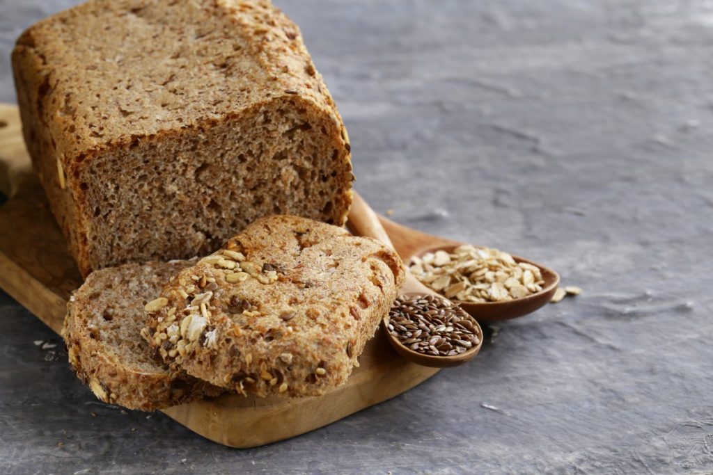 un pane su base di legno e due fette, mestoli con semi di cereali