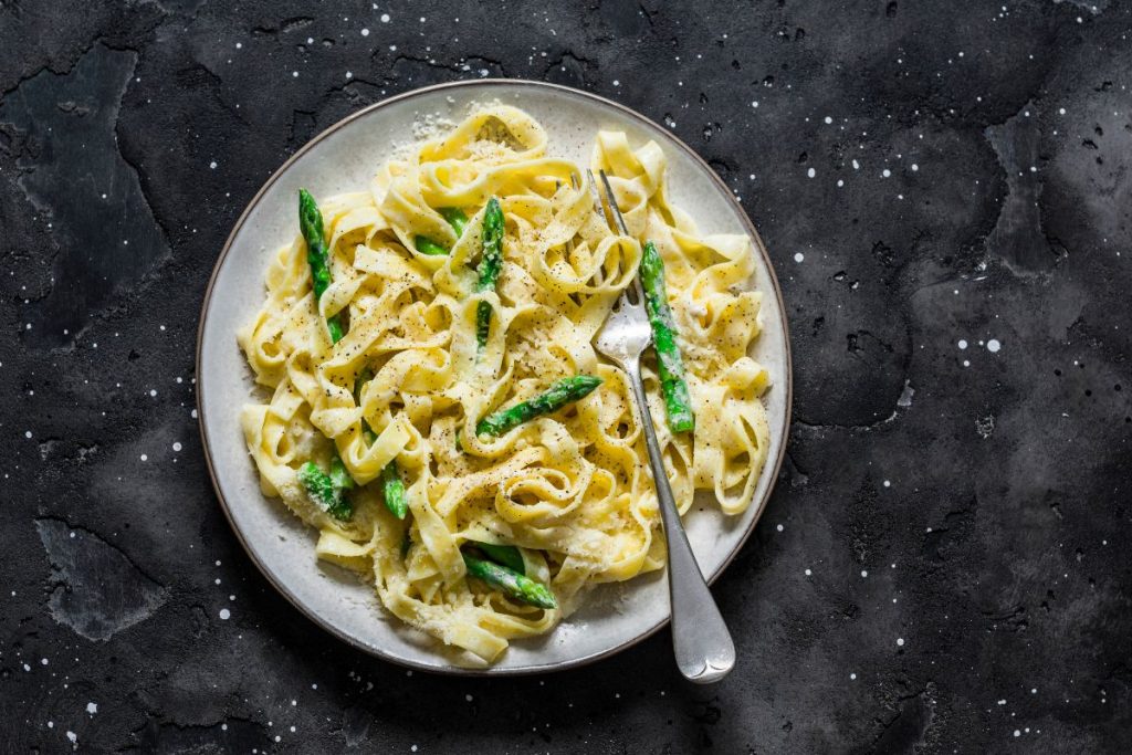 su sfondo nero un piatto bianco con pasta con asparagi croccanti e cremosi