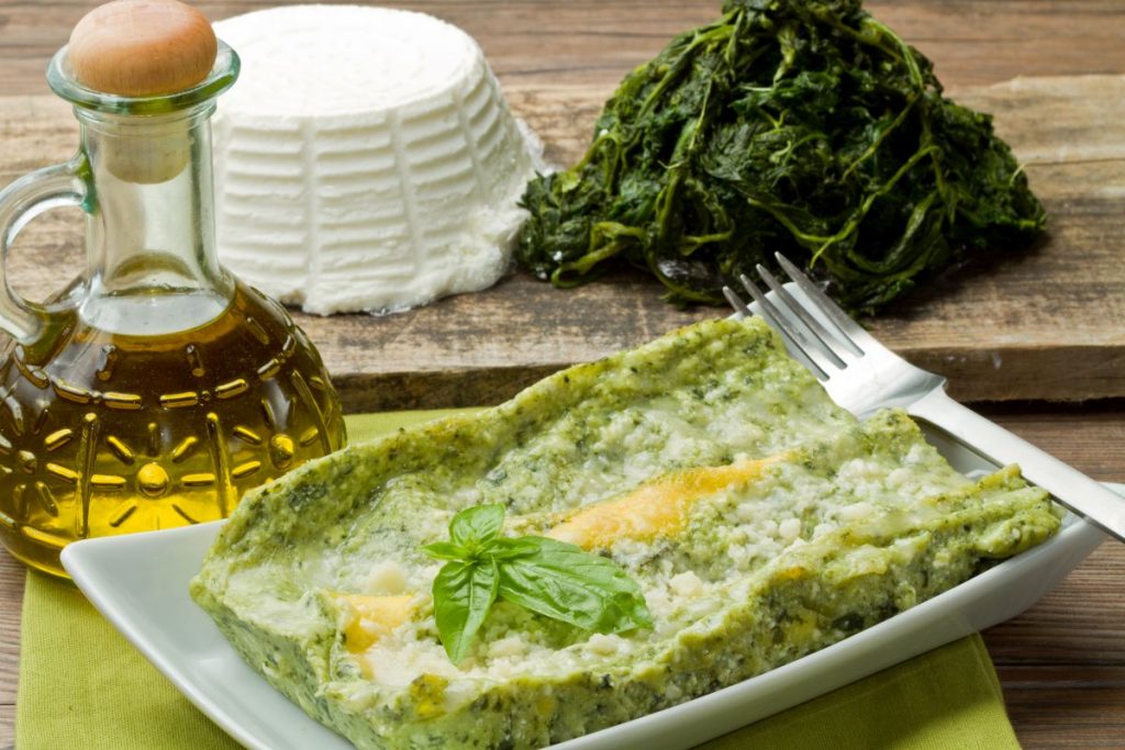 piatto rettangolare con una porzione di lasagna, oliera, ricotta e spinaci accanto