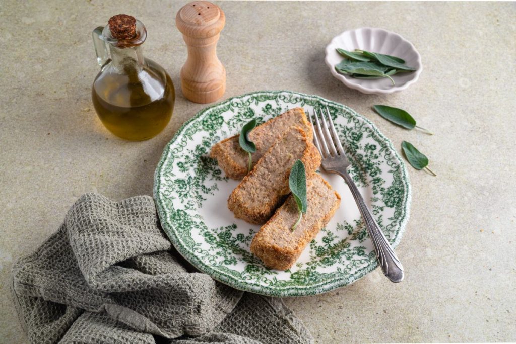 tavola con piatto con 3 fette di polpettone di tonno e canovaccio e olio d'oliva