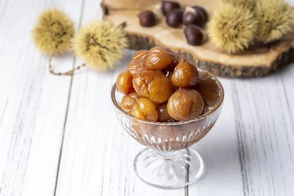 coppa di vetro con marron glaces e dietro vassoio di castagne