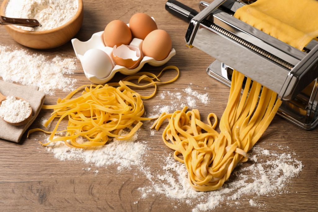 su un tavolo, una macchinetta per tirare la sfoglia della pasta fatta in casa, uova e farina