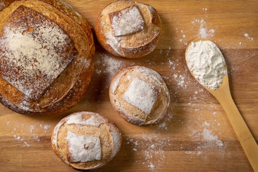 una pagnotta e tre pagnottine accanto a un mestolo di farina