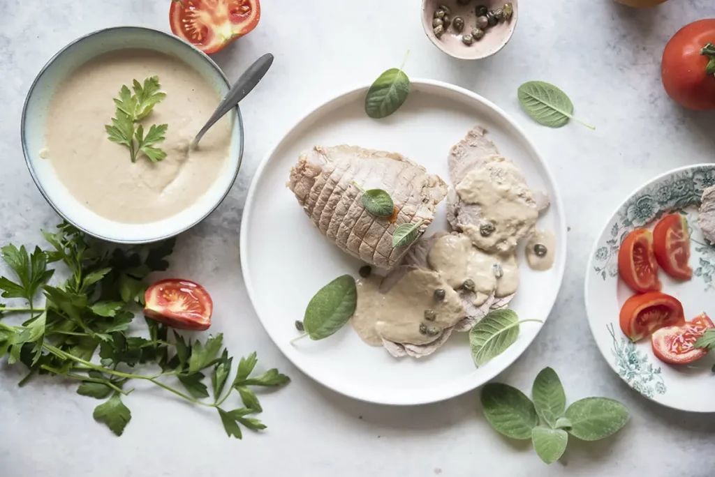 piatto tondo con vitello tonnato, scodella con salsa e pomodori sparsi intorno