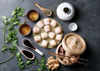 su tavolo di marmo, ricette cinesi con ravioli al vapore in vaporiera di bambù, con piatti di salsa agrodolce e bacchette cinesi . Attorno erbe aromatiche