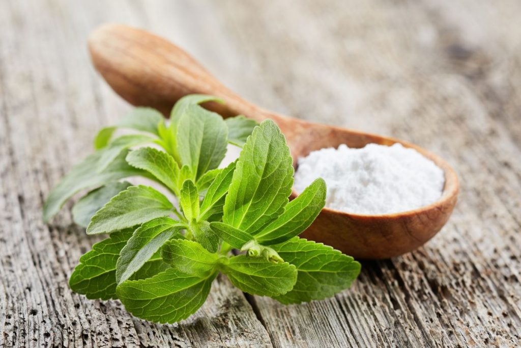 Un ciuffo di foglie di stevia con un cucchiaio in legno colmo di polvere di stevia