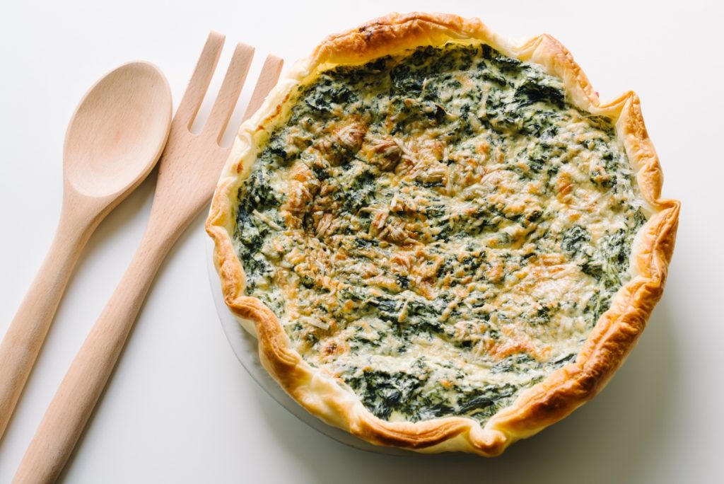 una torta ricotta e spinaci con due mestoli di legno accanto