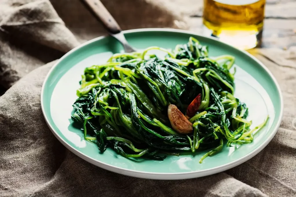 su un tavolo di legno piatto blu con la cicoria ripassata e accanto una bottiglia di olio d'oliva