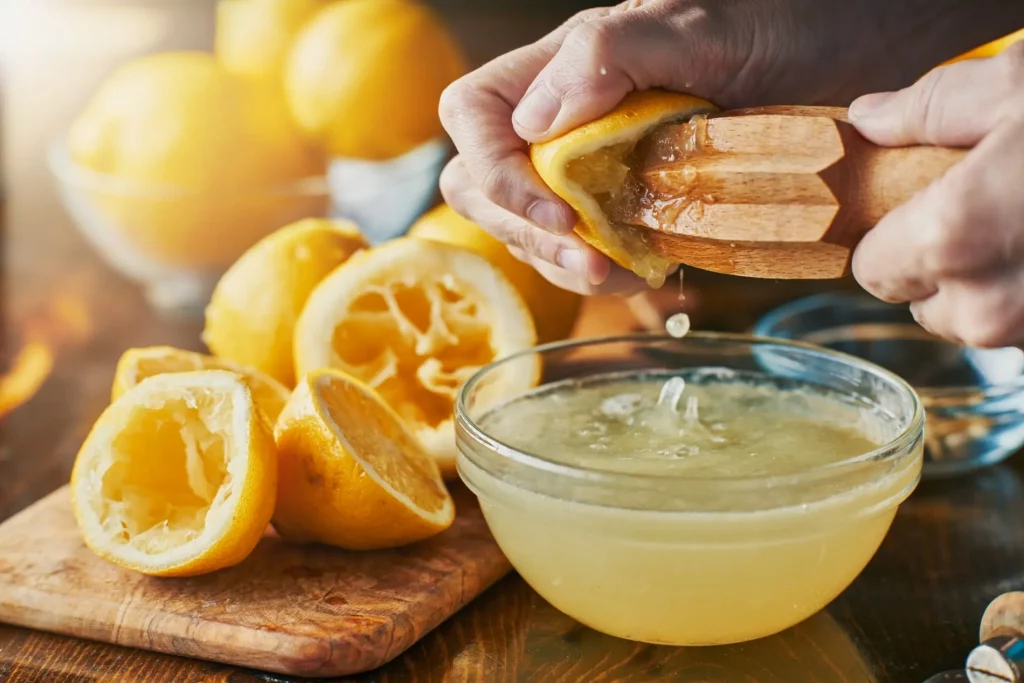 primo piano di mani che spremono limoni per bere acqua e limone al mattino con bucce di limoni