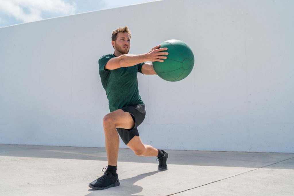 Uomo in allenamento outdoor esegue un affondo laterale con la palla medica