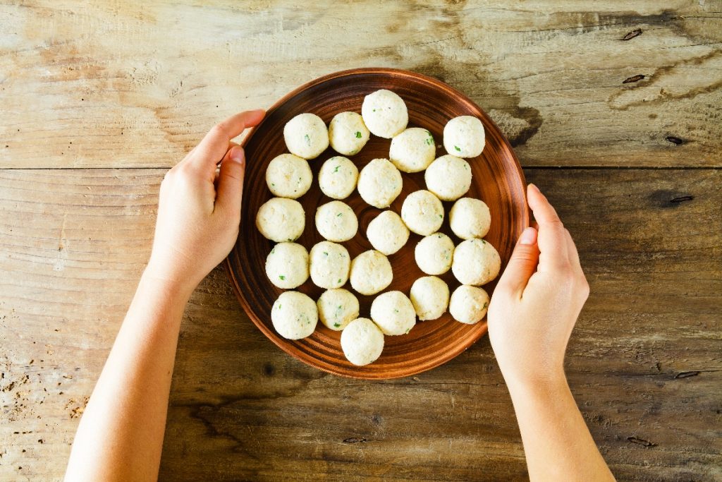 su tavolo di legno. mani di una donna che fa vedere una ciottola con diverse polpette di ricotta prima di infornarle