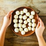 su tavolo di legno. mani di una donna che fa vedere una ciottola con diverse polpette di ricotta prima di infornarle