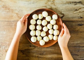 su tavolo di legno. mani di una donna che fa vedere una ciottola con diverse polpette di ricotta prima di infornarle