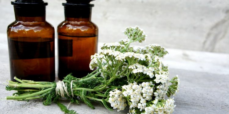 su tavolo di marmo bianco, un mazzo di Achillea millenium e 2 bottiglie maroni di olio essenziale