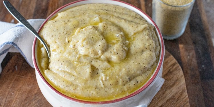 su tavola di legno, ciotola con la polenta taragna e un cucchiaio, accanto un bicchiere di farina di grano saraceno. Sotto la ciotola, c'è un canovaccio bianco