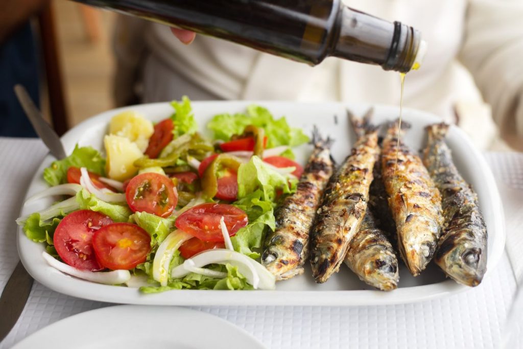 Un piatto con insalata e delle sardine condite con olio di oliva