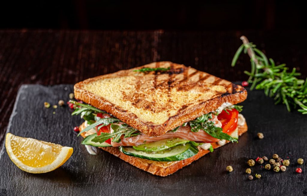 piano di lavoro nero per cucina, panino con pane tostato con avocado, rucola, fette di limone. come tostare il pane velocemente