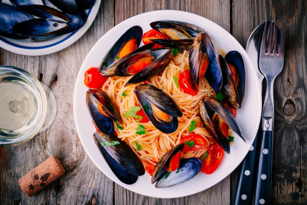 su un piano di cucina primo piano di un piatto di spaghetti con le cozze, un bicchiere di vino, una forchetta e un coltello e un tappo di bottiglia