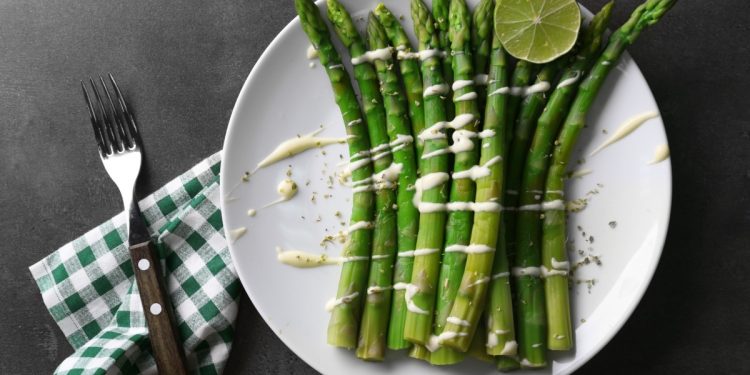 su sfondo nero piatto bianco con asparagi in padella con burro e Parmigiano, sulla sinistra tovagliolo a quadretti bianco e verde