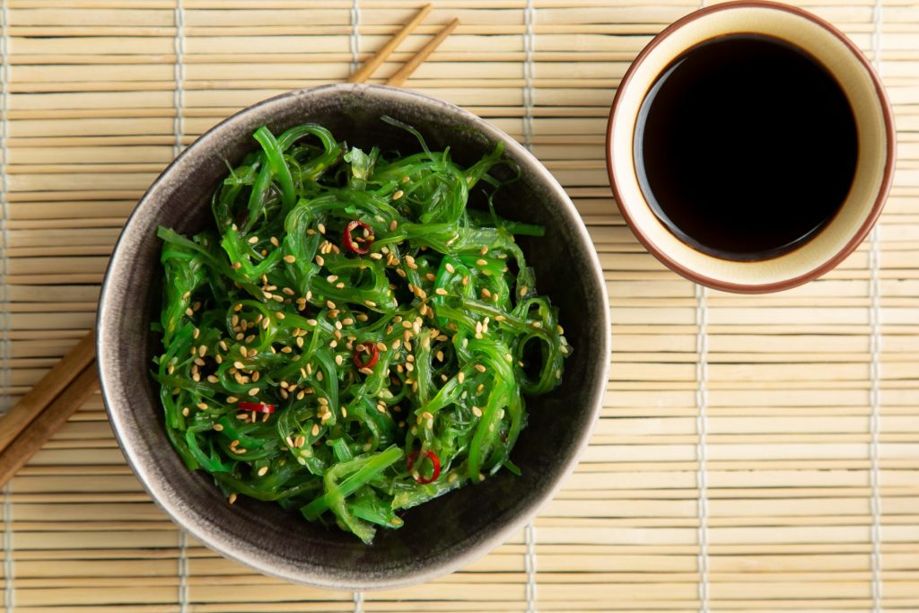 sottopiatti di bambù con una ciottola piena di alga wakame con bacchette giapponesi e salsa di soia