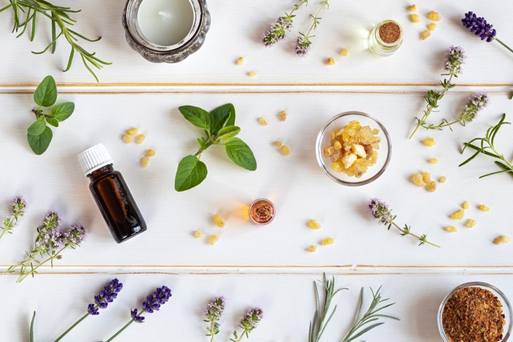 su uno sfondo bianco: una boccia di oli essenziali con lavanda, menta, rosmarino sparso sul tavolo