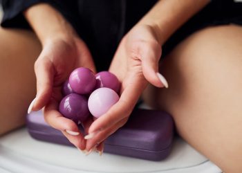 una donna seduta tiene in mano delle palline vaginali rosa e ha un dispositivo elettrico viola accanto a lei