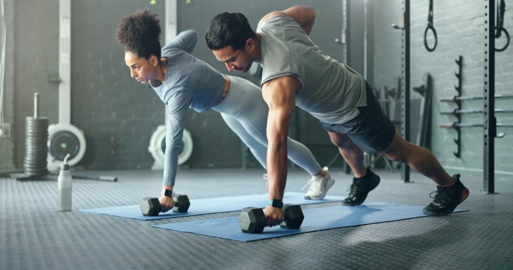 un coppia in palestra con fisico perfetto in posizione di plank che si allena con i pesi