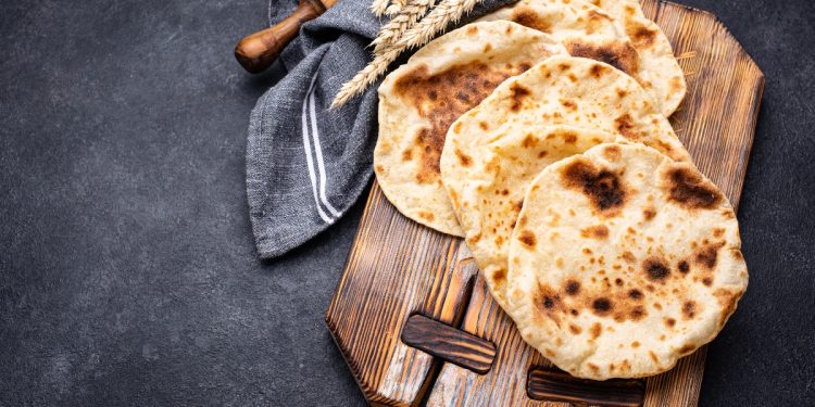 su sfondo nero, tagliere di legno con 4 pani pita, un mattarello