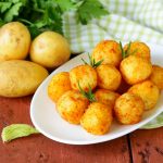 piatto ovale bianco con polpette di patate accanto a tre patate e prezzemolo