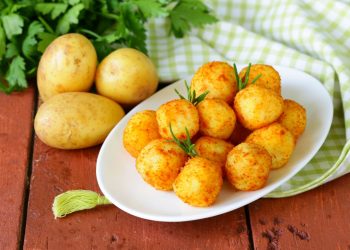 piatto ovale bianco con polpette di patate accanto a tre patate e prezzemolo