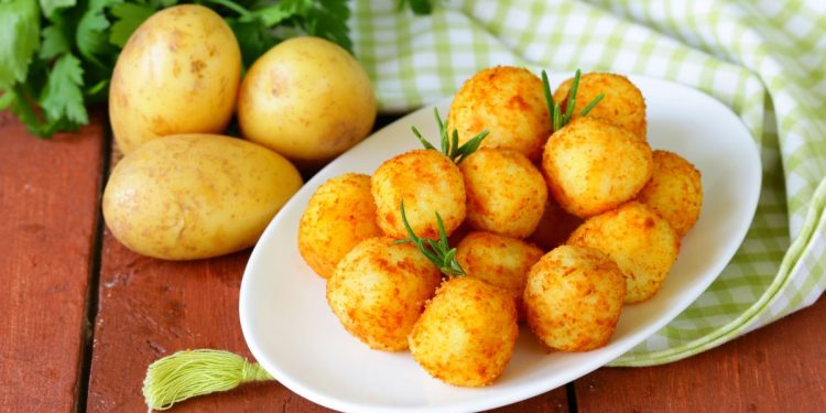 piatto ovale bianco con polpette di patate accanto a tre patate e prezzemolo