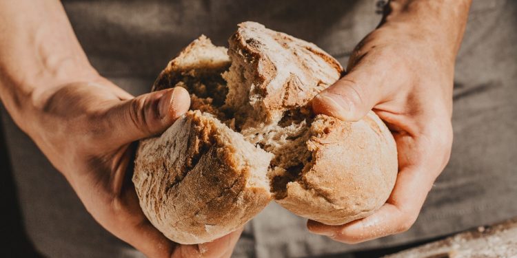 due mani spezzano una forma di pane a metà