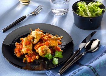 su tavolo apparecchiato, piatto nero con involtini di pesce spada e un bicchiere di acqua e di vino bianco e in una ciotola insalata verde.