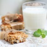 primo piano di barrette proteiche fatte in casa con la frutta secca e dietro un bicchiere di latte