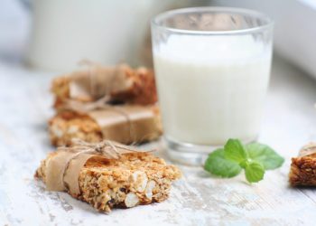 primo piano di barrette proteiche fatte in casa con la frutta secca e dietro un bicchiere di latte